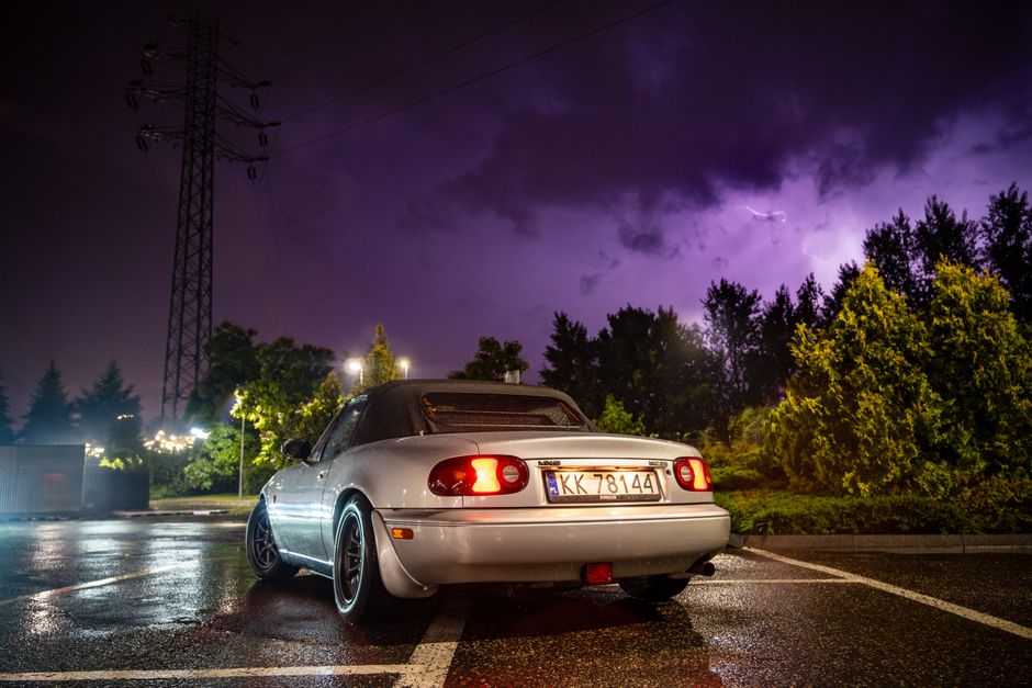 A sleek roadster parked under dramatic stormy skies, captured in Myślenice, Poland during twilight.